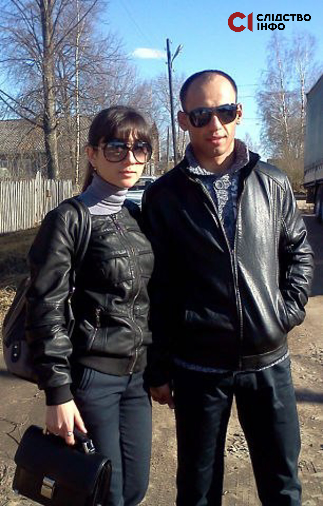 На вулиці стоїть двоє людей у чорному одязі й окулярах: жінка (зліва) і чоловік (справа)